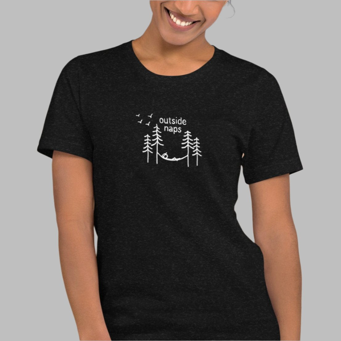 model wearing Black heather tee with hand-drawn illustration of a person laying in a hammock in the trees in white