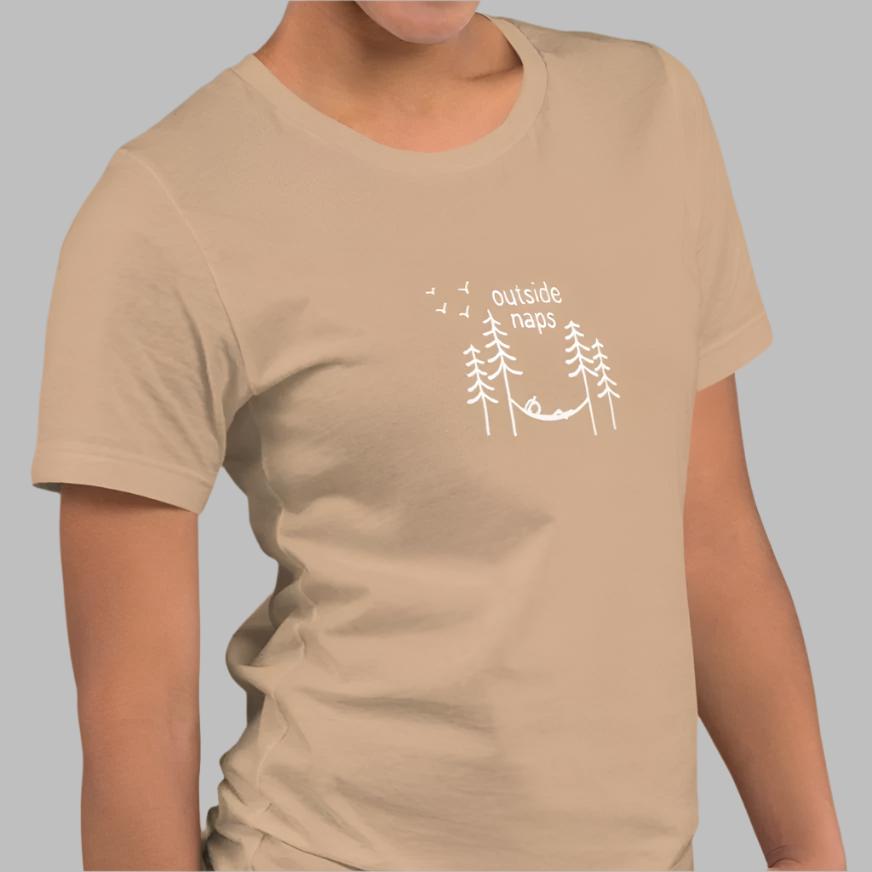 Tan cotton tee with hand-drawn illustration of a person laying in a hammock in the trees in white. On a model